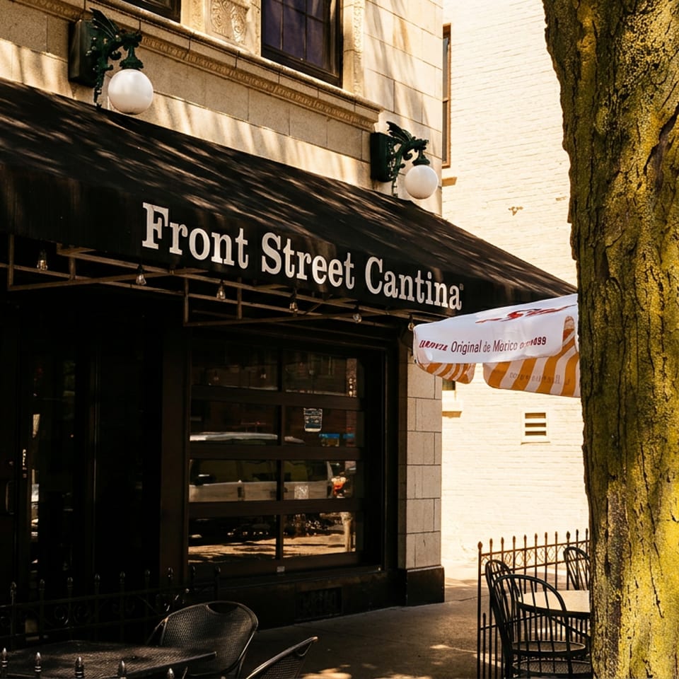 Front Street Cantina restaurant exterior with a black awning, outdoor seating, and a tree in the foreground.