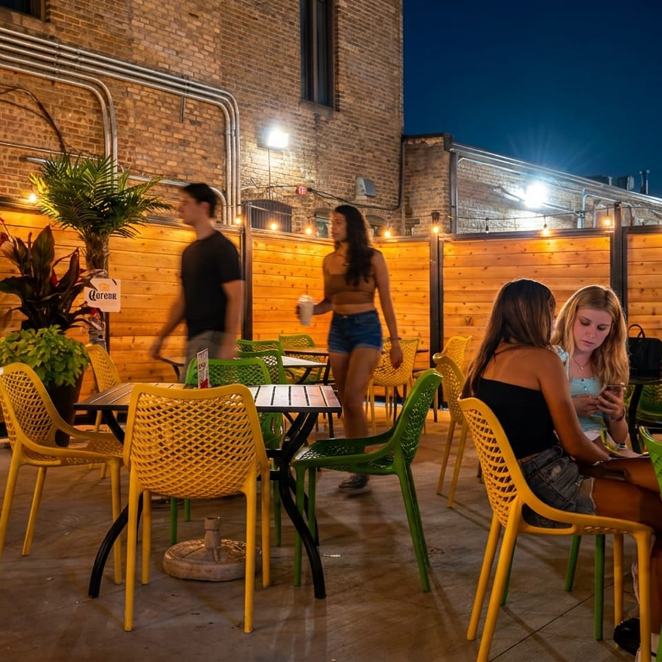 People enjoying an outdoor patio at night with string lights, wooden fences, and colorful chairs.