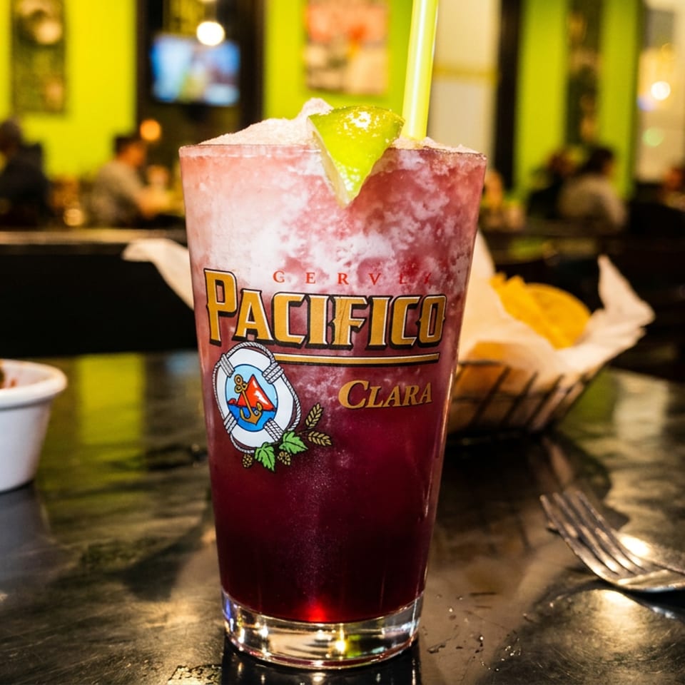 A Pacifico Clara beer cocktail with a lime wedge and straw on a restaurant table.