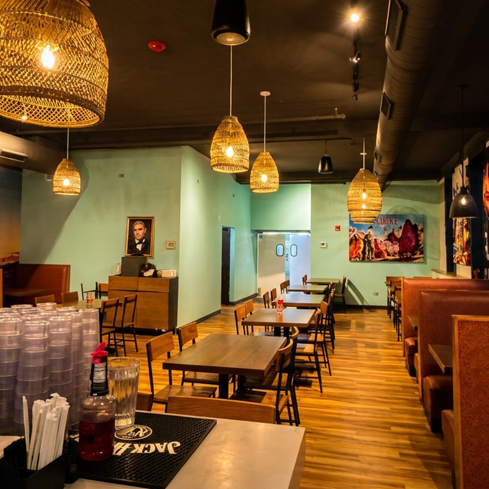 Restaurant interior with wicker pendant lights, light green walls, wooden tables, and brown booths.