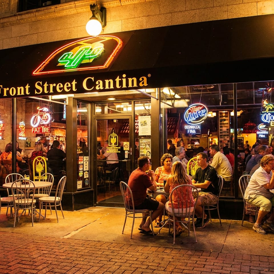 Front Street Cantina at night with people dining outdoors and inside, illuminated by neon signs.