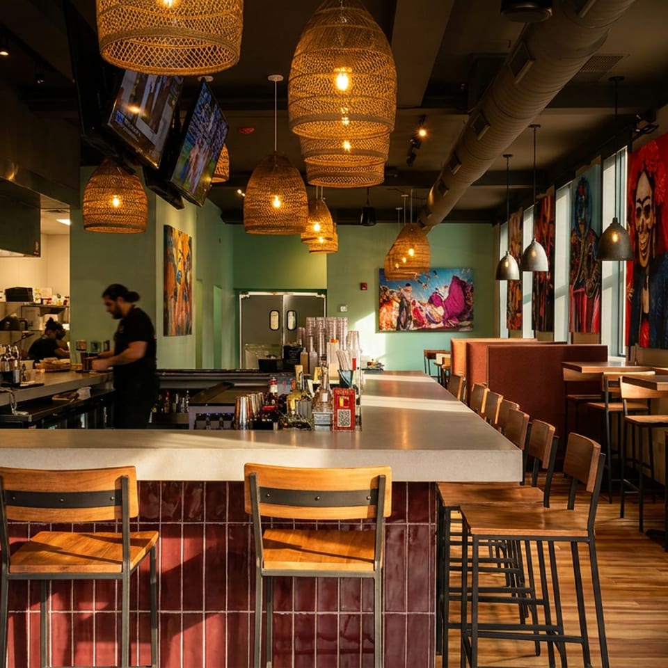 Modern restaurant interior with a long bar, bar stools, dining tables, and colorful wall art.
