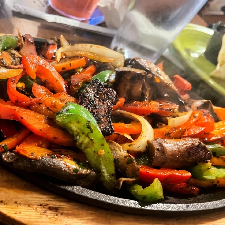 Sizzling fajitas with colorful bell peppers, onions, and meat on a hot cast iron platter.