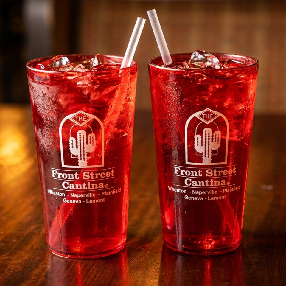 Two red drinks with ice and straws in Front Street Cantina branded glasses on a wooden table.